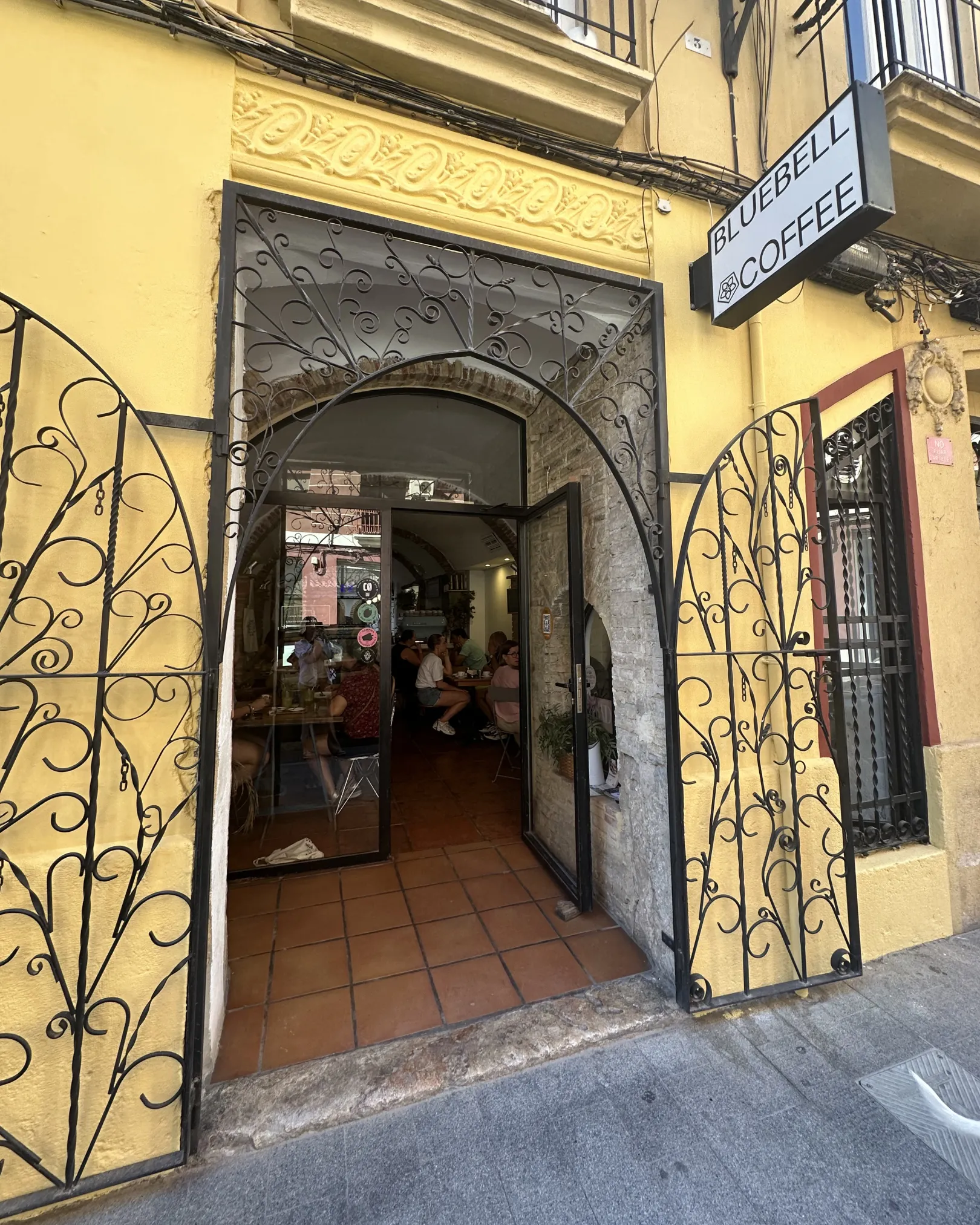 Wrought iron gates and the Bluebell Coffee sign on the yellow facade in Ruzafa, Valencia