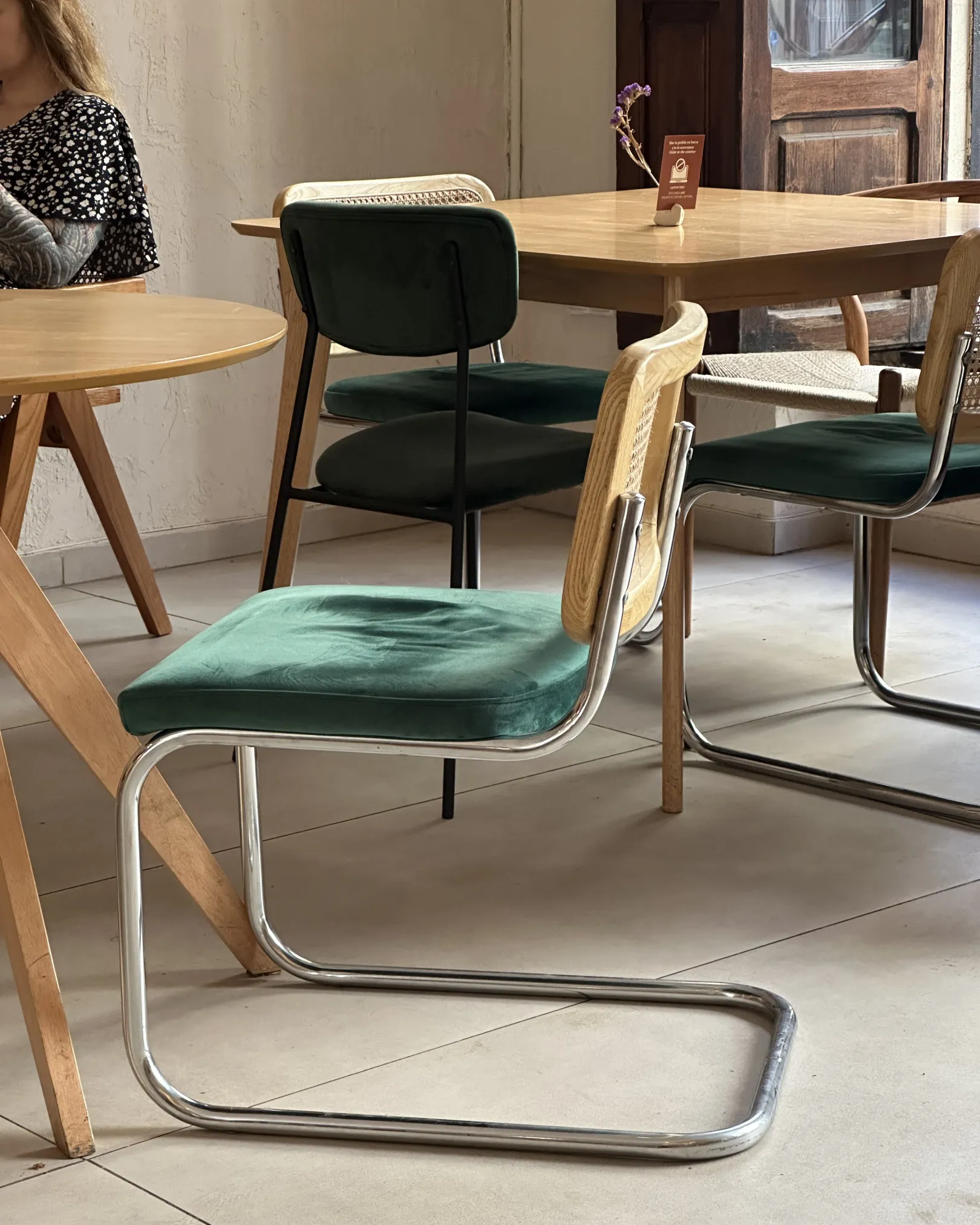 Green velvet chairs and wooden tables beside the antique door at Casa Raíz, Ruzafa, Valencia