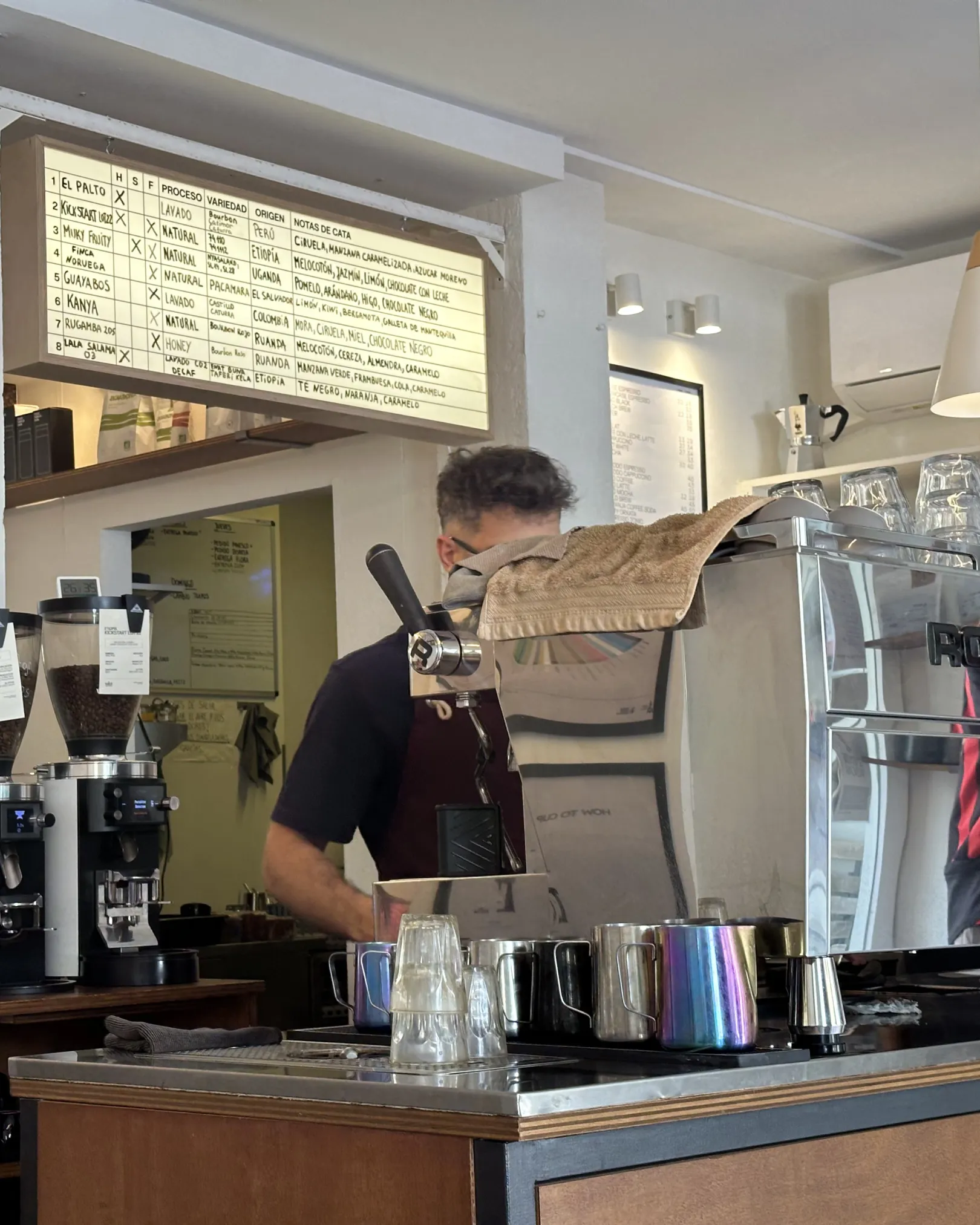 Barista at the espresso machine below the origin board at Tallat Coffee Roasters, El Cabanyal, Valencia